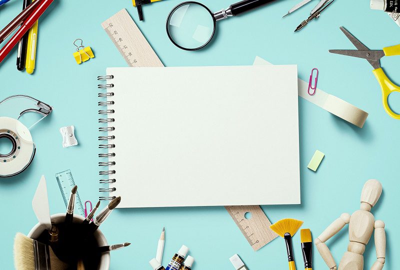 Decorative image of of a blank notepad surrounded by classroom materials.